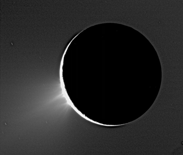 Eisfontänen auf Enceladus Eine helle Sichel bildet sich auf einem schwarzen, kreisrunden Himmelskörper. Der Hintergrund ist dunkel.