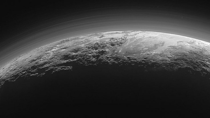 Aufnahme der Oberfläche Plutos gegen die Sonne, Bildquelle: NASA/JHUAPL/SwRI; Lizenz: gemeinfrei Über einer Kraterlandschaft erstreckt sich ein Schimmer im Sonnenlicht.