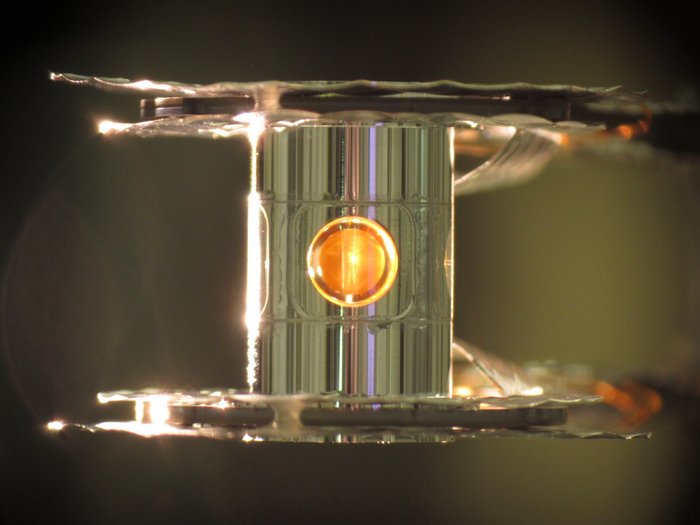 Zylinder mit Kernbrennstoff Transparenter Zylinder, der zwischen zwei Platten eingespannt ist. Im Inneren des Zylinders befindet sich ein goldfarbener, kugelförmiger Hohlraum.
