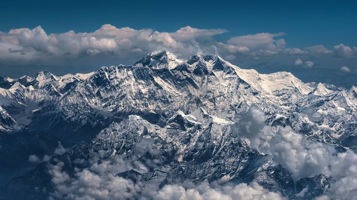Schneebedecktes Gebirgsmassiv mit zahlreichen Gipfeln, umgeben von Wolken