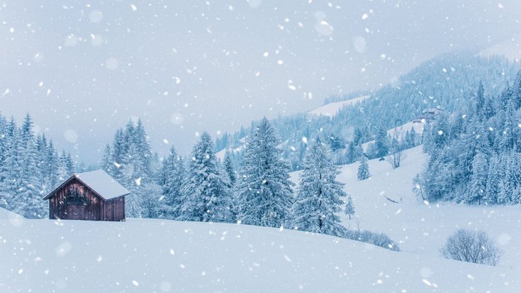 Schneelandschaft mit fallenden Schneeflocken in den Bergen, im Vordergrund eine Holzhütte