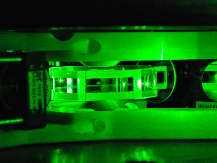 Glaszelle mit gefangenen Atomen Eine flache, kantige Glaszelle mit gefangenen Atomen, hell erleuchtet von grünem Laserlicht.
