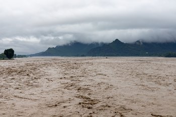 Verschmutztes Wasser eines überfluteten Flusses mit Berglandschaft. 