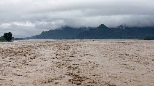 Verschmutztes Wasser eines überfluteten Flusses mit Berglandschaft. 