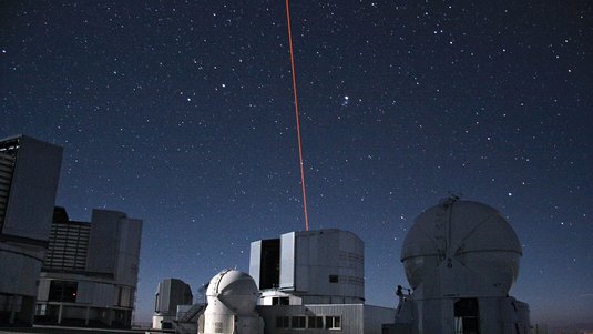 Gebäude in der Dämmerung. Aus einem Dach kommt ein roter Laserstrahl.