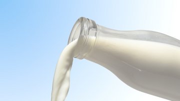 Es fließt Milch aus einer Glasflasche.