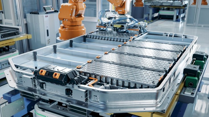 Lithium-Ionen-Batterien | Bildquelle: SweetBunFactory/iStock Metallene Form mit mehreren rechteckigen Fächern in einer Werkhalle, einige de Fächer sind mit Platten gefüllt, auf deren Oberfläche sich kreisförmige Vertiefungen abzeichnen.