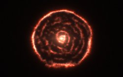 Ein heller Stern im Zentrum ist von spiralförmig angeordnetem Gas  umgeben.