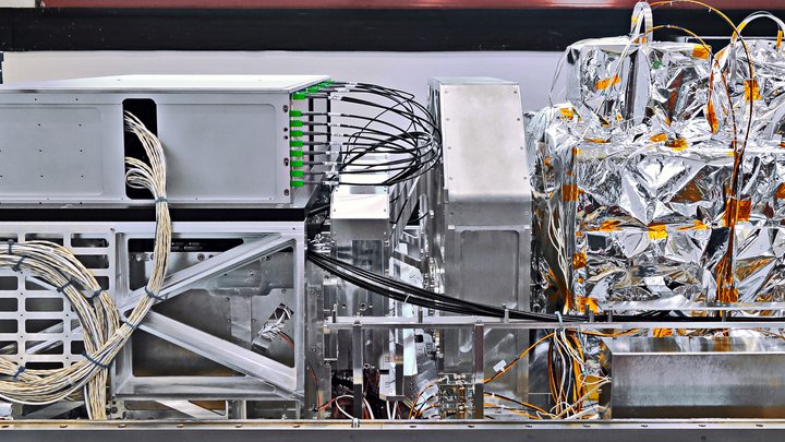GRAVITY ist ein technisches Gerät; auf der fotografischen Aufnahme sind mehrere Boxen zu sehen, die zum Teil mit Kabeln verbunden sind, zum Teil mit Folie verpackt sind.