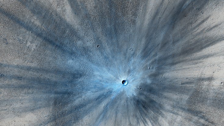 In der Mitte ein sich hell von der Umgebung abhebender Krater mit Zentralerhebung, davon radial ausgehend helle und dunkle Streifen
