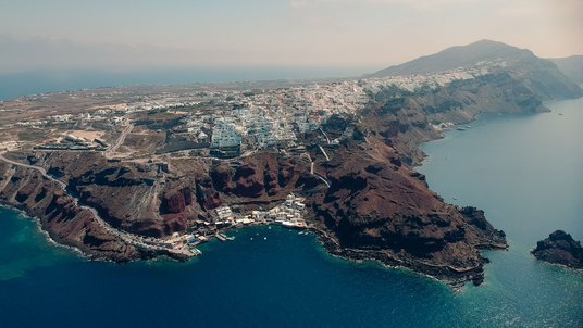 Die Insel Santorin | Bildquelle: ValeriiIavtushenko/iStock Luftaufnahme der Insel Santorin, mit einer engbebauten und felsigen Küste