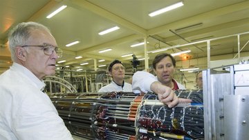 Einige Forscher in weißen Kitteln stehen um eine Anordnung von Kabeln und diskutieren.