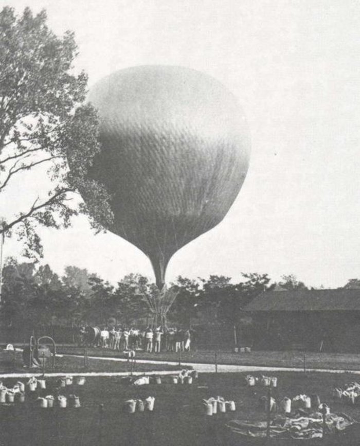 Ballonaufstieg von Victor Hess um 1912 Schwarzweiss-Fotographie: Grosser Heissluftballon steigt auf in einer Gartenlandschaft, viele Besucher schauen zu.
