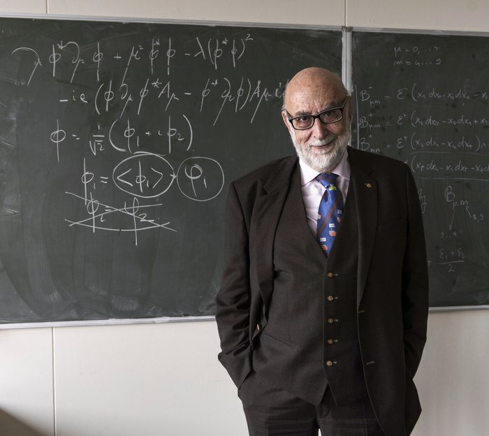 François Englert Ein älterer Herr steht vor einer Schultafel voller Formeln.