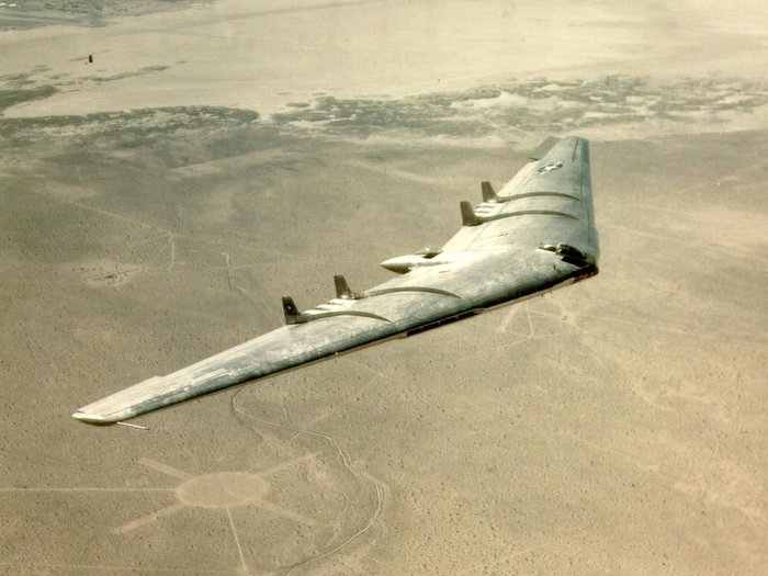 Foto eines fliegenden Nurflügler-Flugzeugs über karger Landschaft.