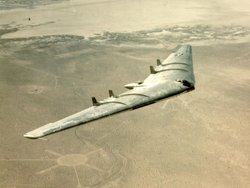 Foto eines fliegenden Nurflügler-Flugzeugs über karger Landschaft.