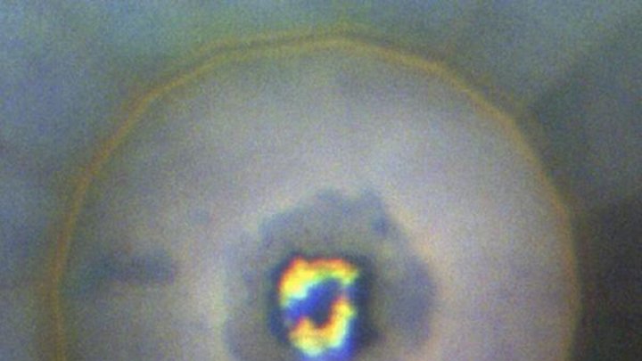 In der Mitte einer kreisförmigen Blase befindet sich eine dunkle Region aus Iridiumhydrid, die mit hellen Flecken aus Wasserstoff durchsetzt ist.