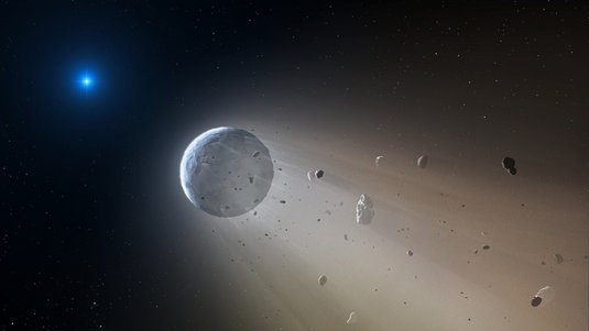 Im Vordergrund ein Zwergplanet, von dem Felsbrocken, sowie Gas und Staub abströmen. Im Hintergrund ein helles, sternartiges Objekt.