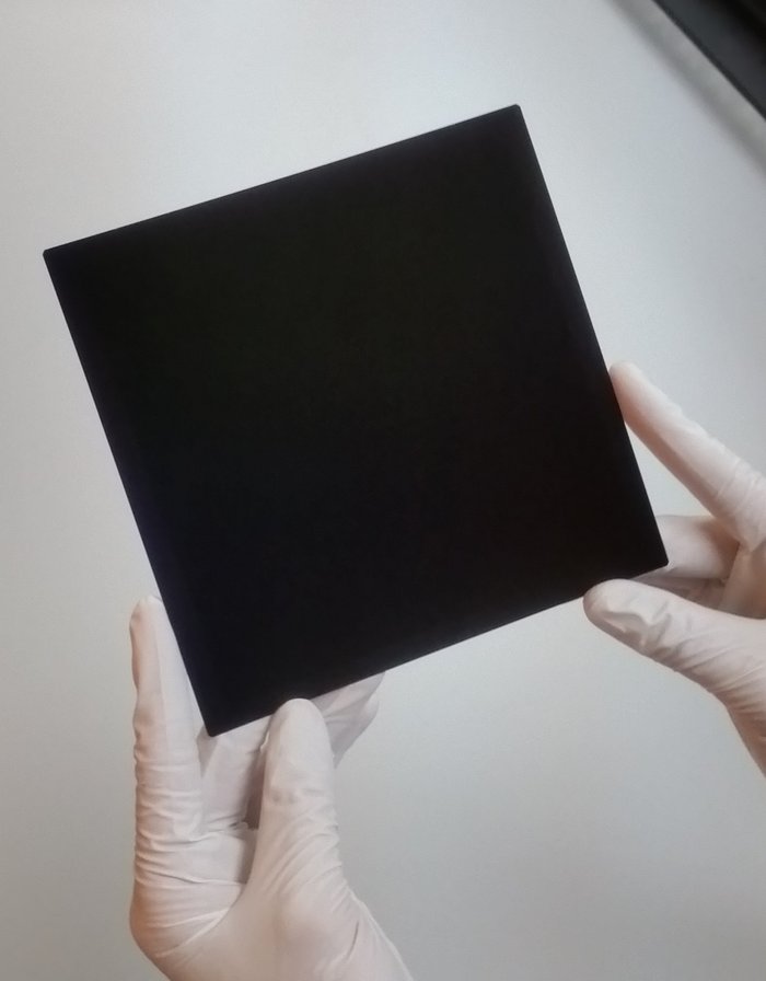 Behandschuhte Hände halten Solarzelle in Form eines schwarzen Quadrates.