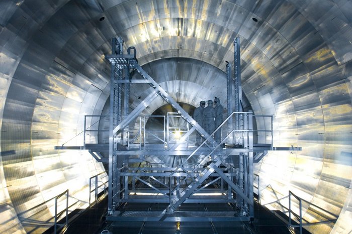 KATRIN-Experiment Die Aufnahme zeigt Wissenschaftler, die auf einem Gerüst vor dem großen, runden KATRIN Experiment stehen.