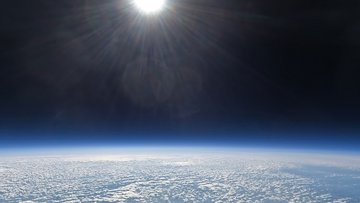 Blick aus der Erdatmopshäre: Am unteren Rand des Bildes ist die Erdoberfläche zu sehen, am oberen Rand eine angeschnittene Sonne - dazwischen ist das dunkle All.