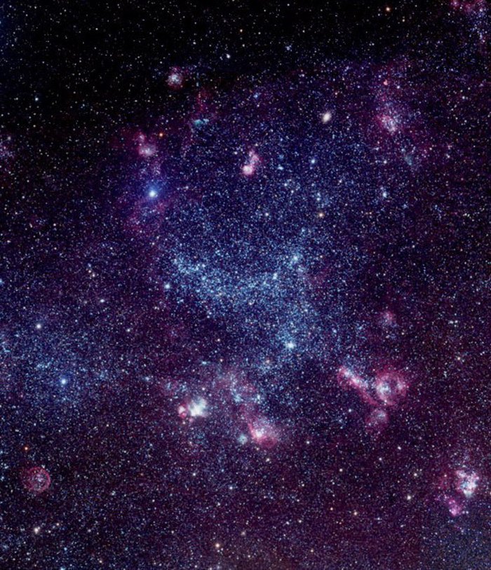 Aufnahme großer Sternhaufen, die zum Teil pinkfarben und violett leuchten. In der Mitte ist eine große bogenförmige Struktur zu erkennen, ein kleinere liegt schrägt darunter.