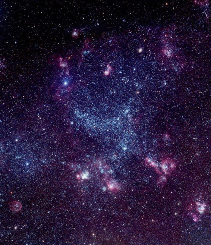 Ausschnitt der Großen Magellanschen Wolke Aufnahme großer Sternhaufen, die zum Teil pinkfarben und violett leuchten. In der Mitte ist eine große bogenförmige Struktur zu erkennen, ein kleinere liegt schrägt darunter.