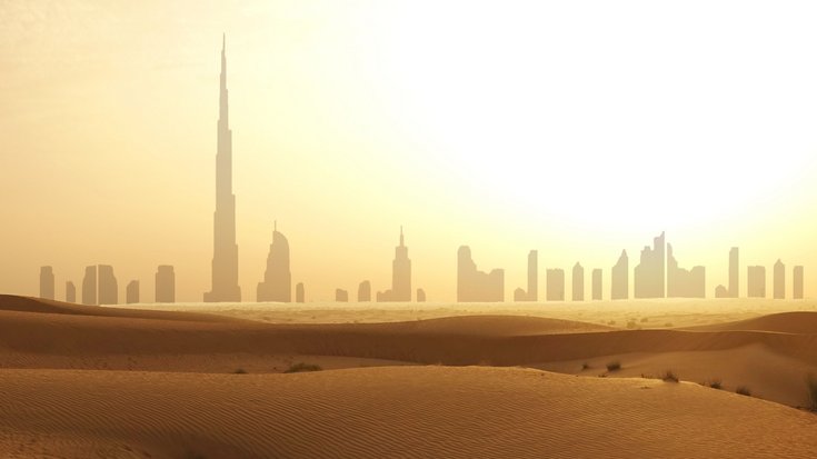 Wüstenlandschaft in Dubai | Bildquelle: adrian825/iStock Silhouette einer Stadt mit vielen Hochhäusern unter einer brennenden Sonne, im Vordergrund Wüstensand