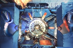Eine große Maschine, in deren Zentrum ringförmig der BaBar-Beschleuniger liegt. Als Größenvergleich steht daneben ein Mann, der in der Höhe nur etwa ein Drittel des gesamten Detektors ausmacht.