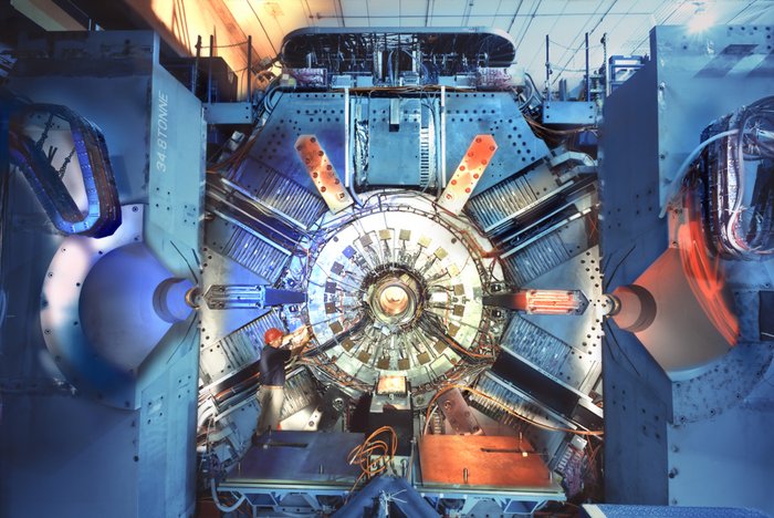 Eine große Maschine, in deren Zentrum ringförmig der BaBar-Beschleuniger liegt. Als Größenvergleich steht daneben ein Mann, der in der Höhe nur etwa ein Drittel des gesamten Detektors ausmacht.