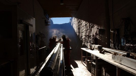 Zwei Männer in Polarkleidung arbeiten an einem Eisbohrkern.