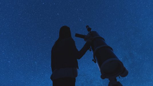Frau mit einem Teleskop unter dem Nachthimmel