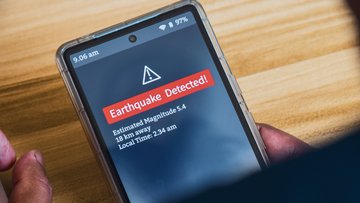 Eine Hand hält ein Smartphone, auf dem eine Erdbebenwarnung erscheint. Darauf steht: Earthquake Detected! Estimated Magnitude: 5,4. 18 km away. Local Time: 2:34 am.