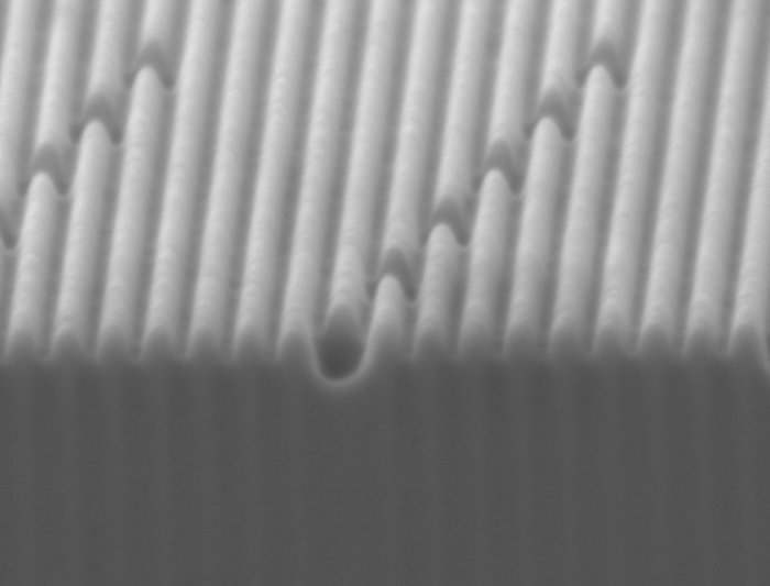 Metafläche aus Silber Vergrößertes leicht unscharfes Bild einer Materialoberfläche mit gleichmäßigen Rillen, in denen teilweise schräg dazu Furchen verlaufen.