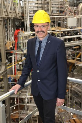 Porträt des Wissenschaftlers Robert Wolf in einer Maschinenhalle mit Schutzhelm