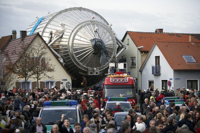 Das Spektrometer wird angeliefert 2006 wurde das Spektrometer für KATRIN an das Karlsruher Institut für Technologie gebracht – und brauchte für den Weg von Deggendorf nach Karlsruhe rund 8600 Kilometer meist auf dem Seeweg. Ein Transport über Land war aufgrund der Größe des Spektrometers nicht möglich. Die letzten paar Kilometer legte KATRIN dann auf einem Schwertransport zurück, auf dem Bild zu sehen ist der Weg des Spektrometers durch den Ort Leopoldshafen, bei dem KATRIN genau zwischen zwei Häuser zu passen scheint.