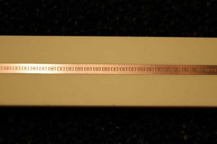Metallstruktur für Metamaterial Kupferfarbener Metallstreifen mit Enprägungen auf einem hellen Untergrundmaterial.