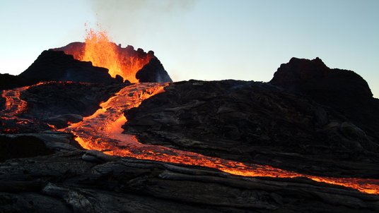 Aus einem Vulkan schießt glühende Lava und fließt den Vulkan herab