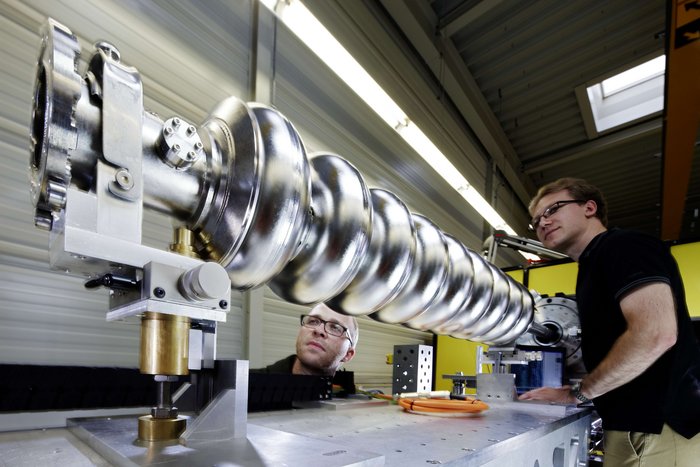 Inspektion der Innenfläche Zwei Menschen beobachten eine Metallröhre, die auf einem Labortisch befestigt ist. Längs der Röhrenachse verläuft eine Stange.