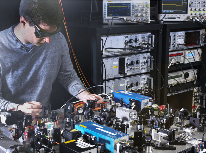 Laseraufbau Dieses Bild zeigt einen Wissenschaftler mit Laserschutzbrille, der an einem Tisch mit vielen optischen Elementen steht.