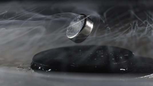 Silbernfarbener Ring, der über einer schwarzen Plattform schwebt, umweht von Luftschwaden