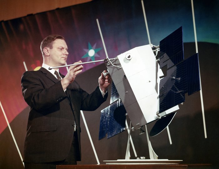 Ein Mann im Anzug hantiert an einem etwa kühlschrankgroßen Modell eines Weltraumteleskops herum.