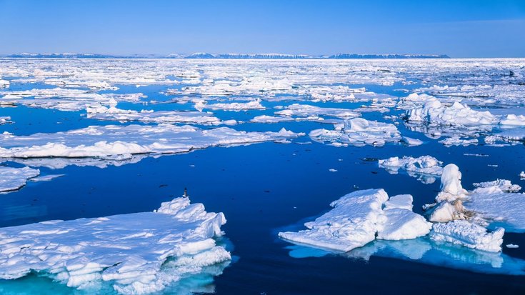 Eisschollen im Meer, darüber ein blauer Himmel
