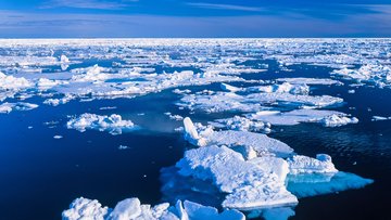 Mehrere Eisschollen im Meer unter blauem Himmel