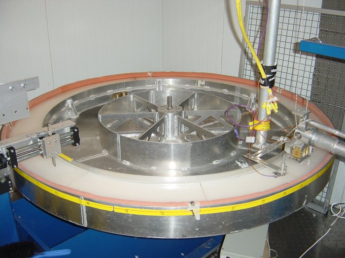 Skibelagtester (Tribometer) Ein etwa 1 Meter durchmessender Ring mit 10 Zentimeter Breite. Auf dem Ring befindet sich eine Eisschickt. An einer Stelle ist ein Halte- und Messarm mit einem Stück Ski angebracht.