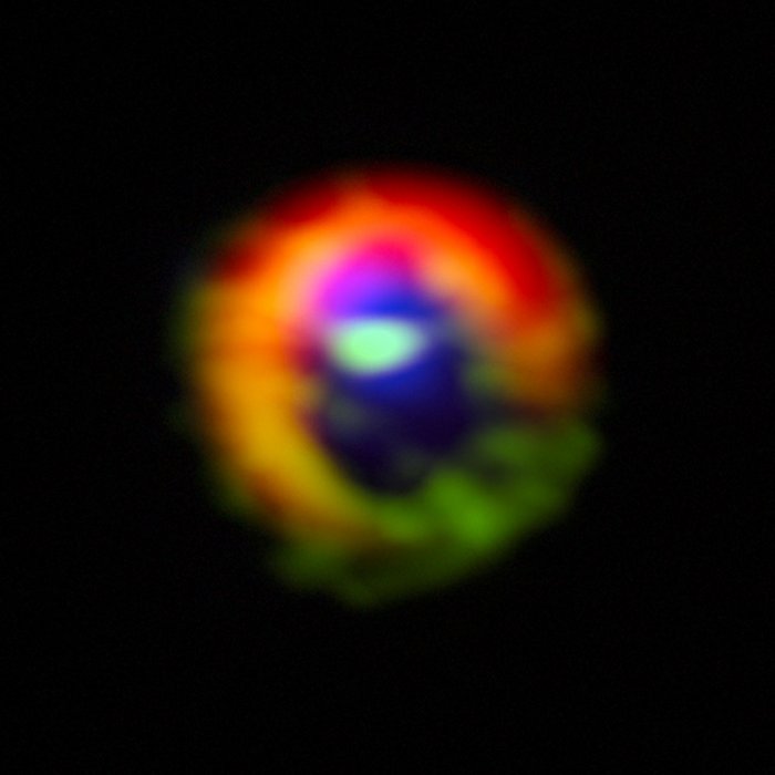 Staub- und Gasscheibe um HD 142527 Der Stern ist als heller Fleck in der Bildmitte zu erkennen, darum sind diffuse Flecken in verschiedenen Farben angeordnet.