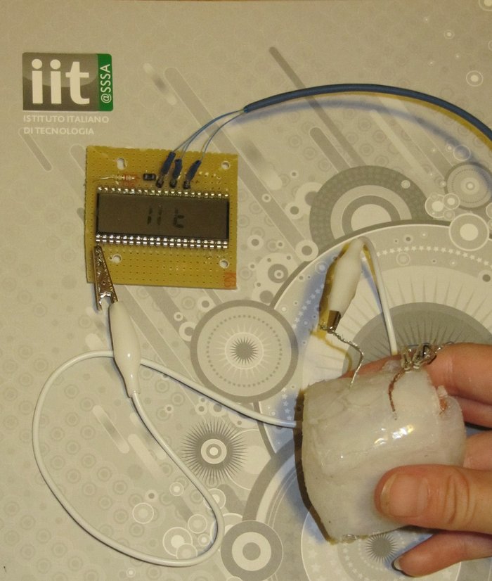 Prototyp eines Schwammgenerators Eine Hand hält unten rechts einen hellen Plastikwürfel, von dem aus ein Kabel nach links oben führt, wo es mit einer Klemme an einer Platine mit Sensor befestigt ist. Von der Platine geht ein weiteres Kabel ab.