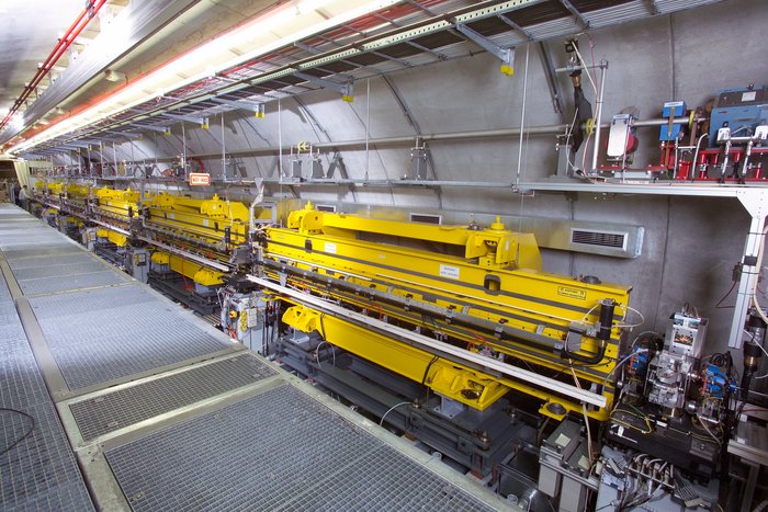 Undulator bei FLASH Blick ins Innere eines Tunnels. Auf der linken Seite ein Gehweg mit Gitterboden, auf der rechten Seite der Undulator, der im Wesentlichen aus zwei übereinander positionierten, länglichen Metallkästen besteht. Drumherum einige weitere technische Komponenten, Kabel und Beleuchtung.