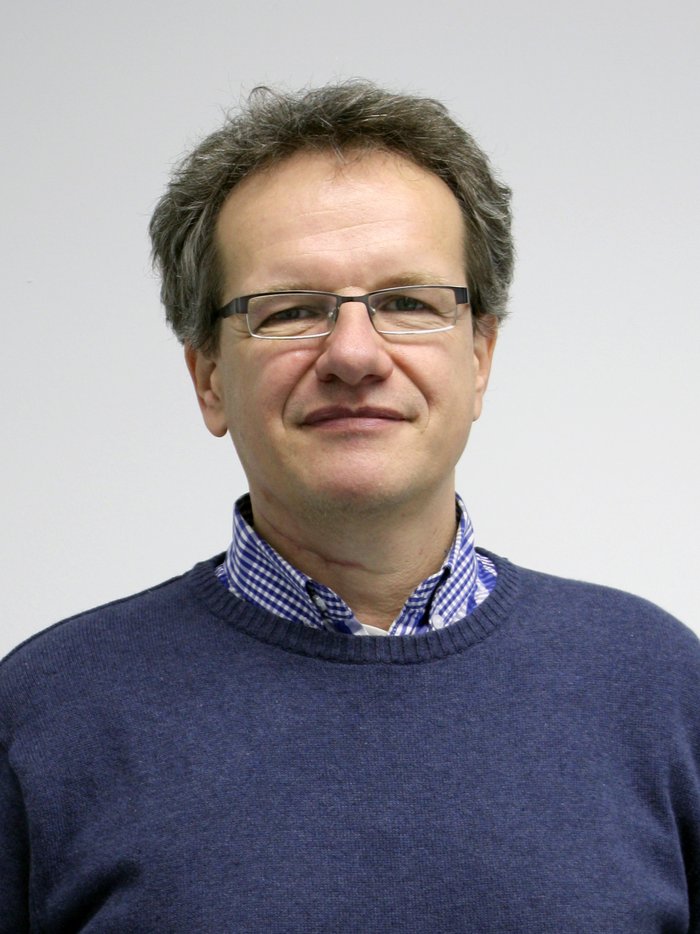 Christoph Hugenschmidt Vor hellem Hintergrund steht ein Mann mittleren Alters mit Brille.