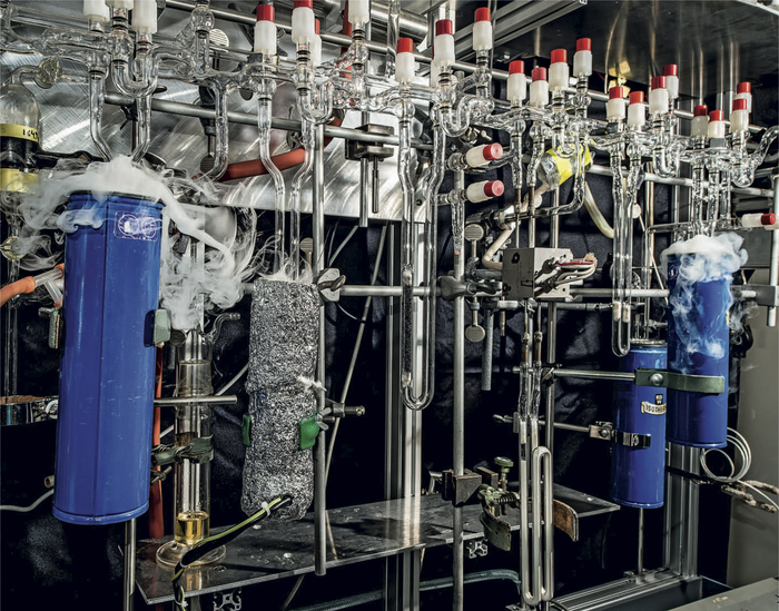 Anlage zur Gasanalytik Aufbau mit vielen gläsernen und silbrig gänzenden Röhren, oben einige Ventile, links und rechts je ein schmaler, hoher Behälter, aus dem es Dampf wabert.